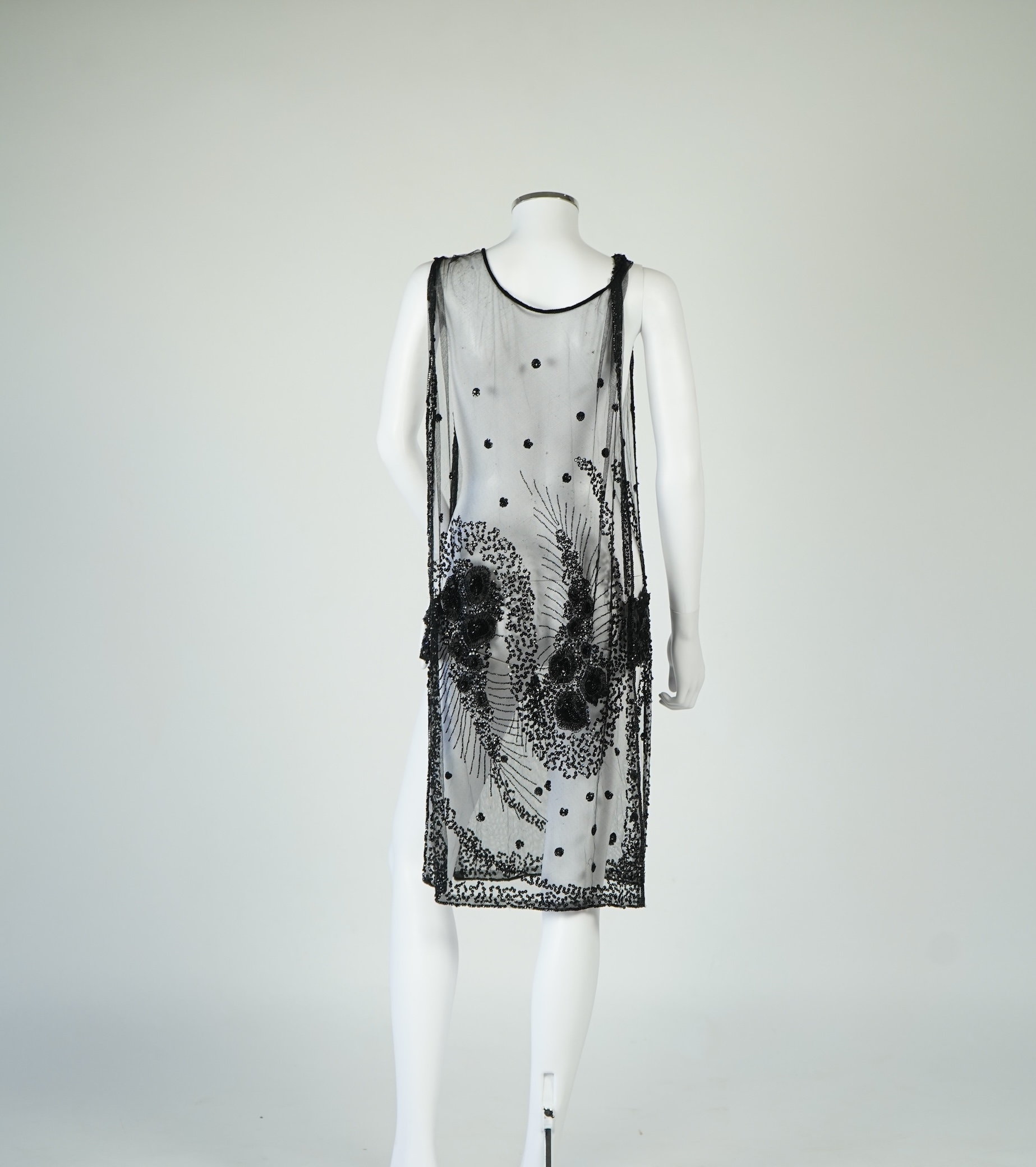 A 1920's black sequin on net tabard, with floral decoration and two side sequinned straps. Length 97cm. Condition - a few sequins have detached but are in a bag for re-attaching.